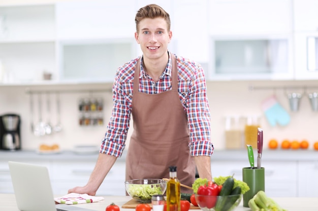 Hombre guapo cocinando ensalada de verduras en la cocina