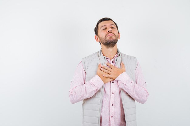 Hombre guapo cogidos de la mano en el pecho en chaleco, camisa y mirando confiado,