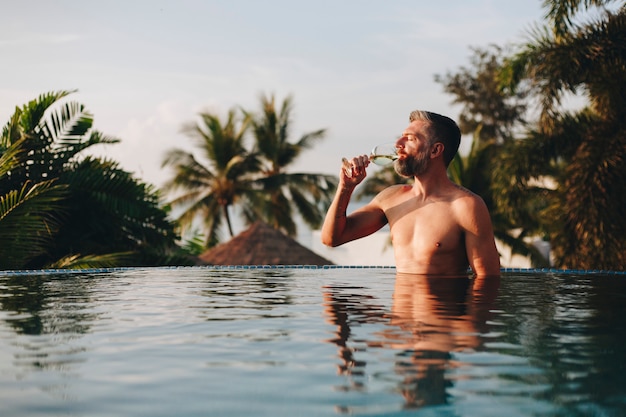 Hombre guapo con una copa de vino en la piscina