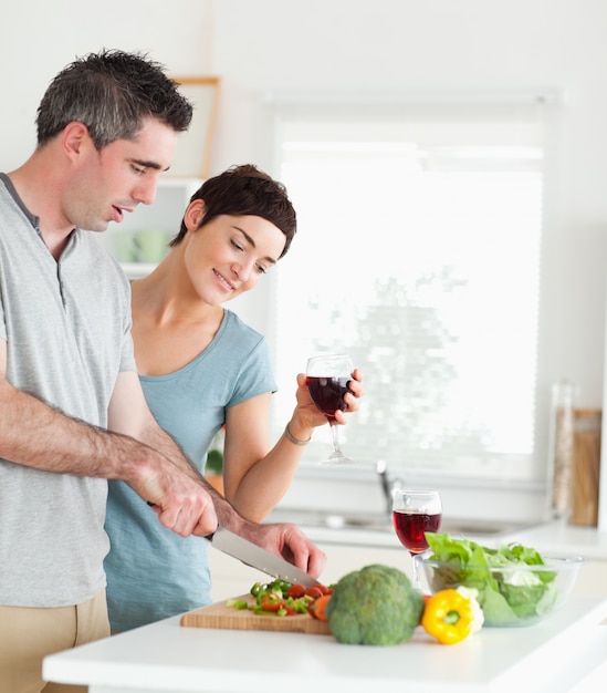 Hombre guapo cortar verduras mientras la mujer está mirando