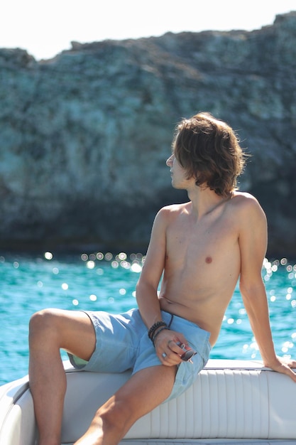 Hombre guapo en la cubierta de un yate de lujo relajándose en un viaje de vacaciones de verano en Menorca