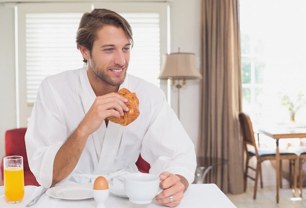 Hombre guapo desayunando en su bata de baño