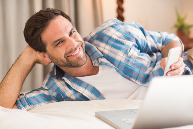 Hombre guapo descansando en su cama con la computadora portátil