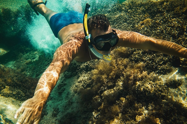 Un hombre guapo divirtiéndose en las vacaciones de verano y explorando el fondo marino durante el buceo en el mar.