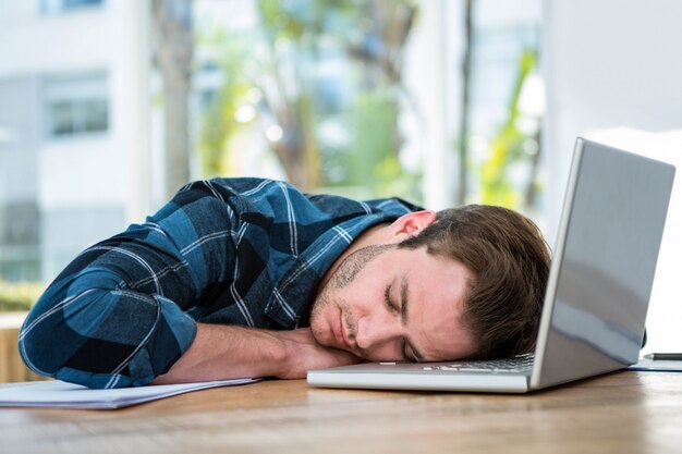 Hombre guapo durmiendo en la computadora portátil en una oficina brillante