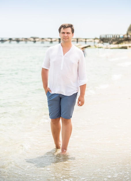 Hombre guapo elegante en camisa blanca caminando por la orilla del mar