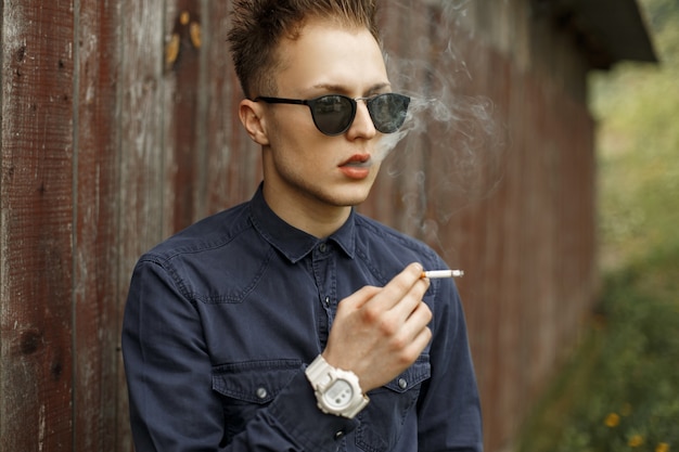 Hombre guapo elegante fumando un cigarrillo cerca de una pared vintage