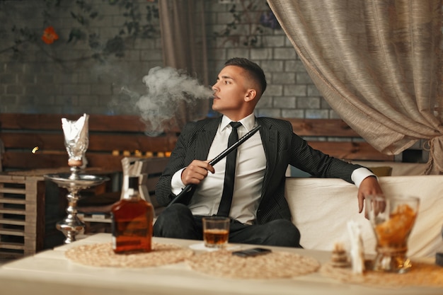 Hombre guapo elegante en un traje fumando una pipa de agua