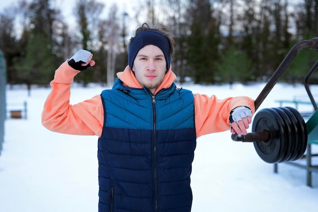 Hombre guapo entrenando al aire libre en el día frío de invierno en el gimnasio muestra bíceps en el parque mirando a la cámara