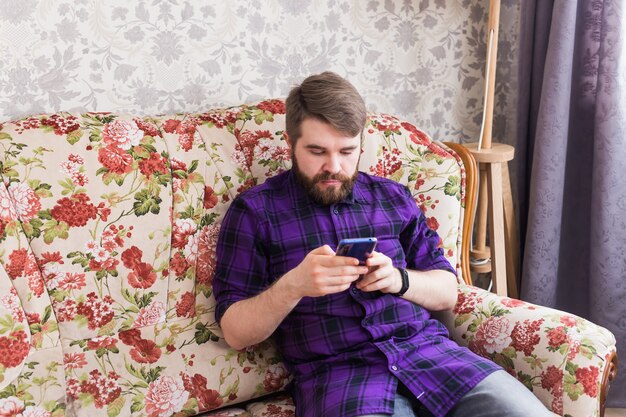 Hombre guapo enviando mensajes de texto con su teléfono inteligente en la sala de estar