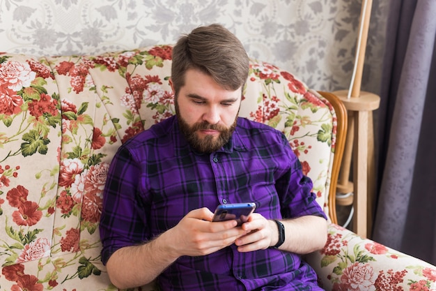 Hombre guapo enviando mensajes de texto con su teléfono inteligente en la sala de estar