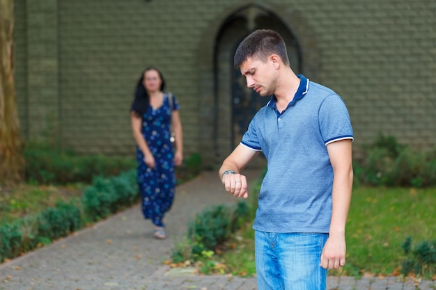 Foto hombre guapo está esperando a la chica en la calle y mira su reloj detrás de él