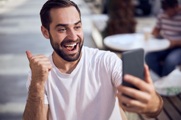 Hombre guapo está hablando en el teléfono inteligente de cerca al aire libre