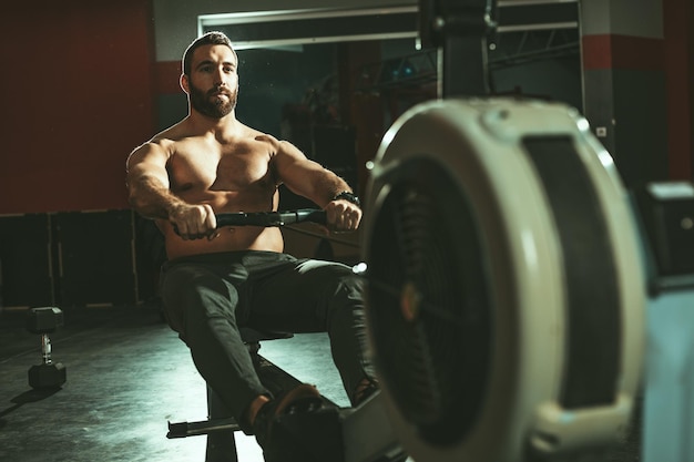 Un hombre guapo está haciendo ejercicio. Tira de la máquina de remo en el gimnasio.