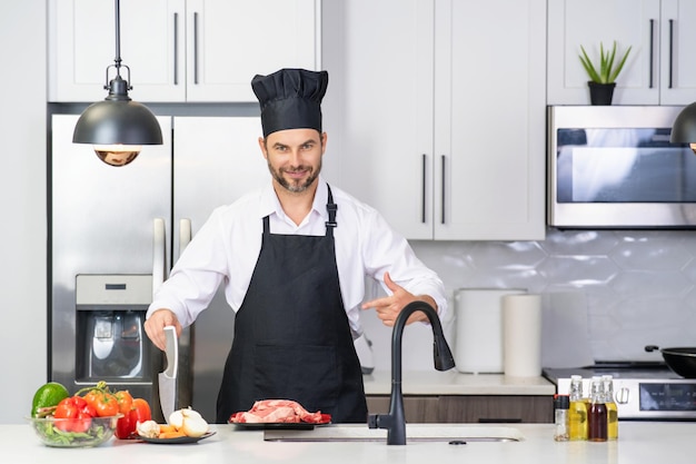 Hombre guapo está preparando comida en la cocina hombre guapo maduro de mediana edad cocinando carne en la cocina