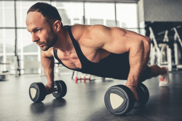 Hombre guapo está trabajando con pesas en el gimnasio.