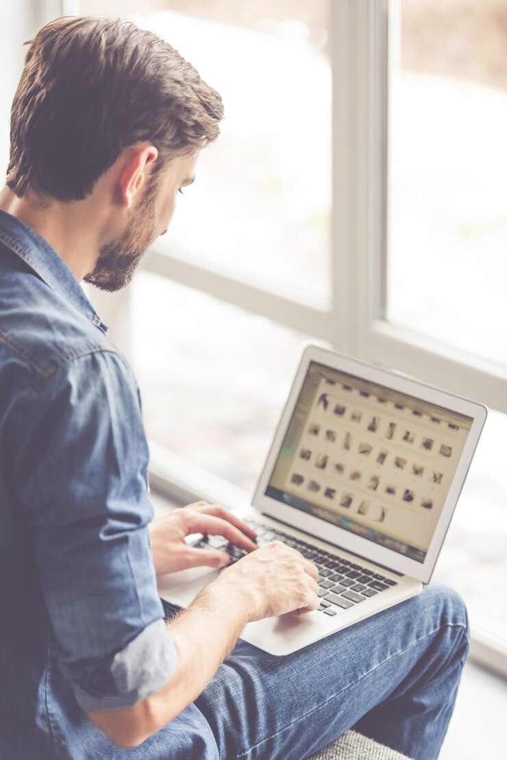 Foto hombre guapo está usando una computadora portátil mientras está acostado en el sofá en casa