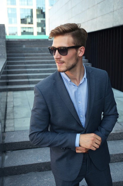 Hombre guapo con estilo en traje elegante y gafas de sol en la calle.