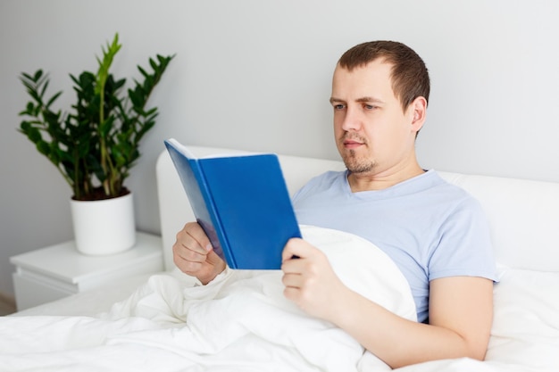 Hombre guapo feliz acostado en la cama y leyendo un libro