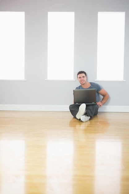 Hombre guapo feliz apoyado contra la pared usando la computadora portátil