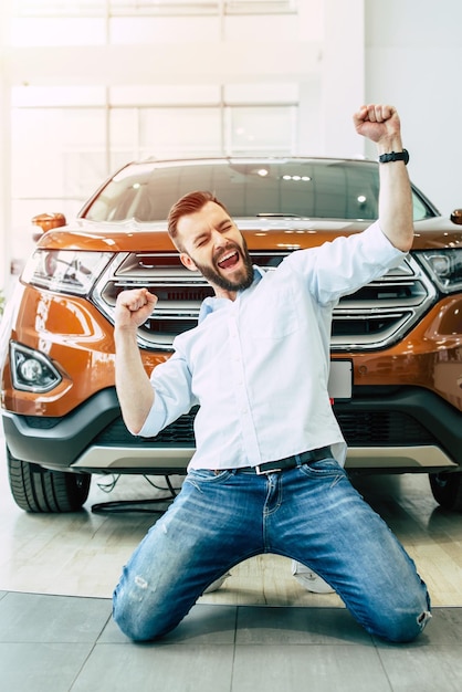 Foto hombre guapo feliz comprando un auto blanco nuevo en el concesionario y bailando en el piso contra el auto