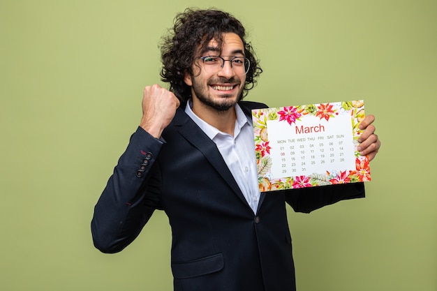 Hombre guapo feliz y emocionado en traje con calendario de papel del mes de marzo