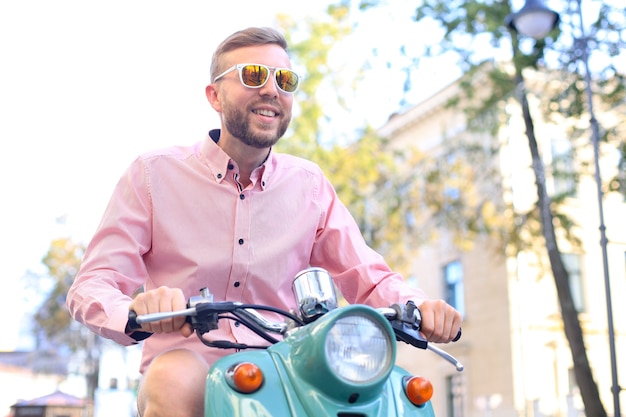 Hombre guapo feliz montando en scooter en la ciudad.