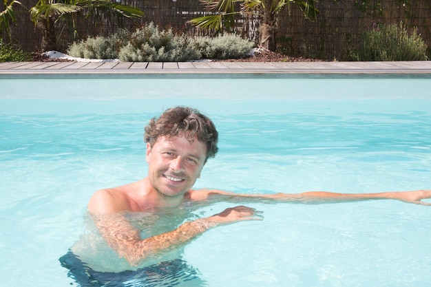 Hombre guapo feliz en la piscina en concepto de vacaciones