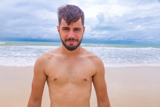 Hombre guapo feliz en la playa de vacaciones Chico joven en la playa sonriendo a la cámara