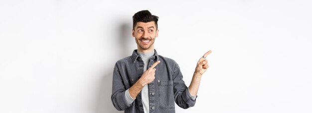 Hombre guapo feliz sonriendo y apuntando a la izquierda en la pancarta que muestra un producto fresco de pie sobre fondo blanco
