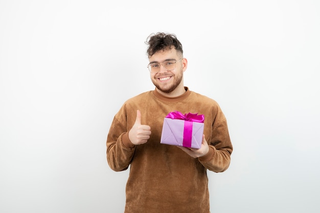 Hombre guapo feliz sosteniendo su regalo de vacaciones y dando pulgar hacia arriba.