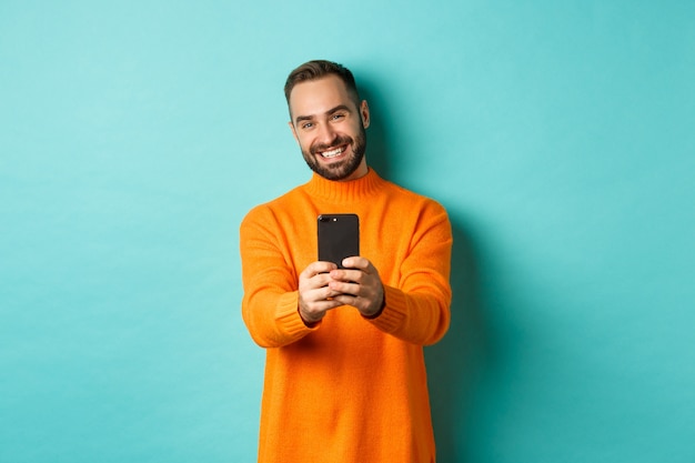 Hombre guapo feliz tomando fotos en el teléfono móvil, tomar fotografías con la cámara del teléfono inteligente, de pie