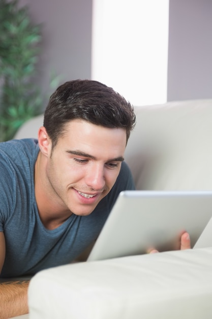 Foto hombre guapo feliz tumbado en el sofá con tableta