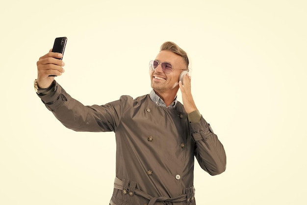 Un hombre guapo feliz usa un teléfono inteligente escuchando música en auriculares aislados en una llamada de video blanca