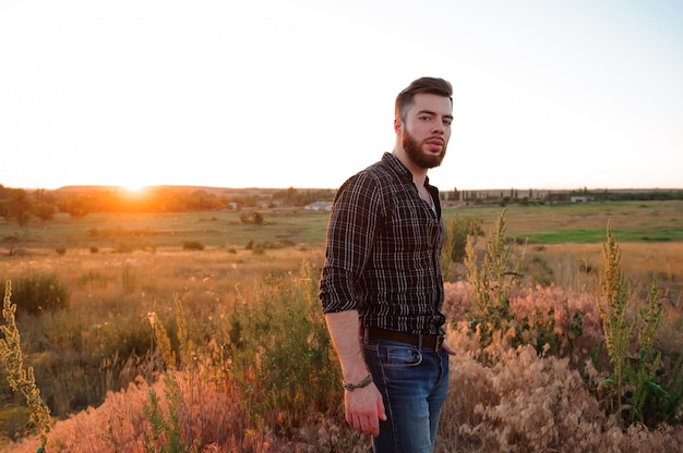 Hombre guapo en el fondo del atardecer. Joven está mirando la puesta de sol. Viajero con mochila