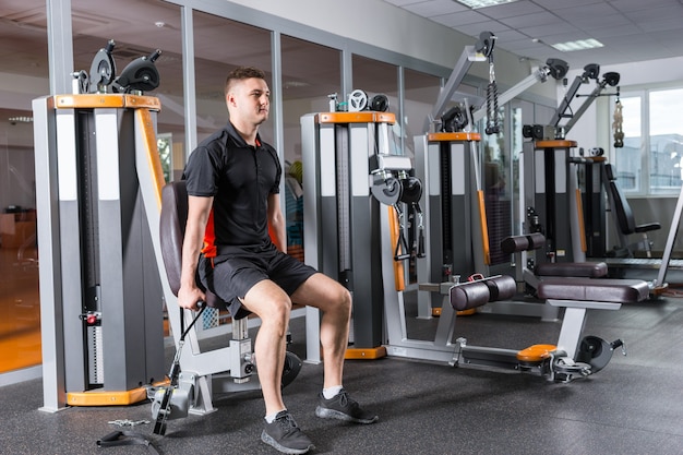 Hombre guapo en forma entrenando en una máquina moderna y trabajando en la sala de gimnasio en el centro de fitness