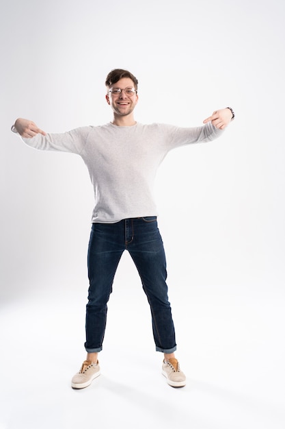 Hombre guapo con gafas asombrado y sonriendo a la cámara mientras presenta con la mano aislada en blanco