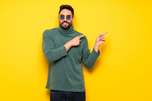 Hombre guapo con gafas de sol asustado y apuntando hacia el lado