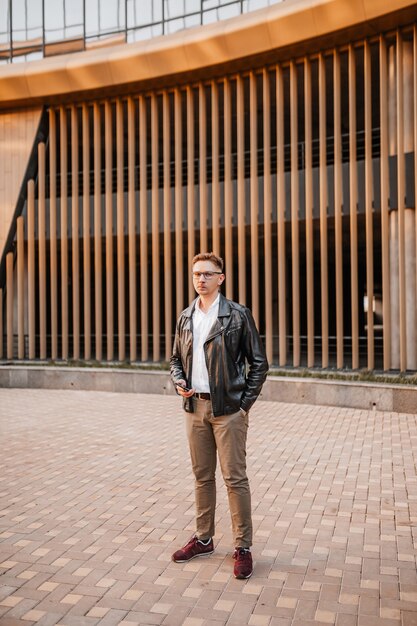 Hombre guapo con gafas con un teléfono inteligente en la calle de una gran ciudad. Empresario hablando por teléfono sobre fondo urbano