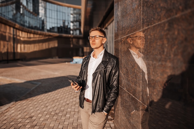 Hombre guapo con gafas con un teléfono inteligente en la calle de una gran ciudad. Empresario hablando por teléfono sobre fondo urbano