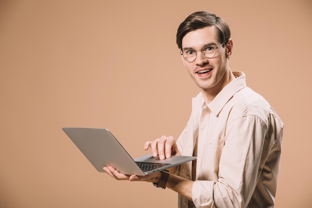 Hombre guapo en gafas usando laptop aislado en beige