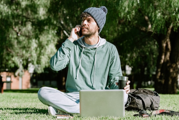 Un hombre guapo con gorro llamando con su teléfono móvil mientras toma un café. Concepto: vida nómada digital