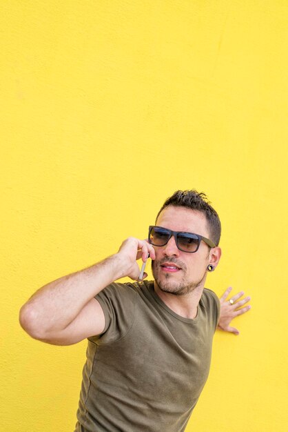 Hombre guapo hablando por teléfono inteligente mientras está de pie contra la pared amarilla