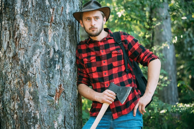 Hombre guapo con hacha Leñador de hombre guapo con un hacha grande examina el árbol antes de talar Leñador de hombre fuerte con un hacha en una camisa a cuadros