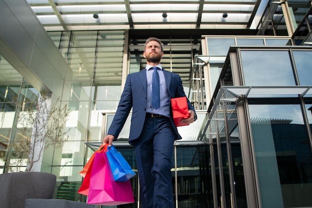 Hombre guapo haciendo compras en la ciudad. Retrato de hombre de negocios en traje con bolsas de la compra.