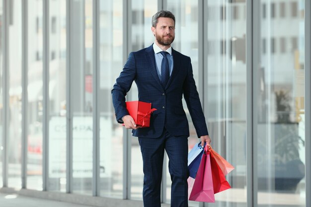 Hombre guapo haciendo compras en el hombre de negocios de la ciudad que lleva bolsas de compras después del trabajo en