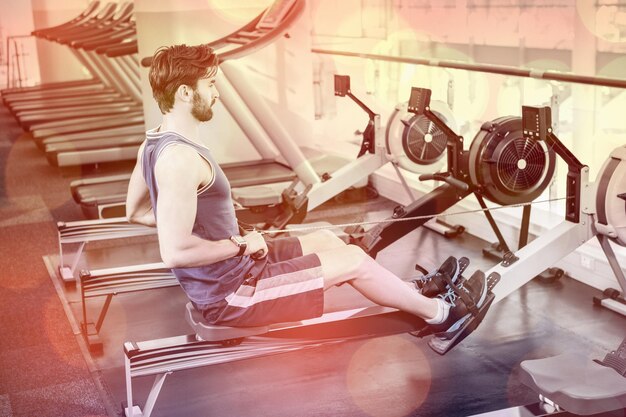 Foto hombre guapo haciendo ejercicio en la máquina de dibujo en el gimnasio