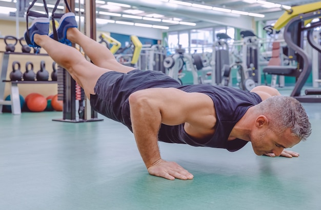 Hombre guapo haciendo entrenamiento de suspensión dura con correas de fitness en un gimnasio. Concepto de estilo de vida saludable y deportivo.