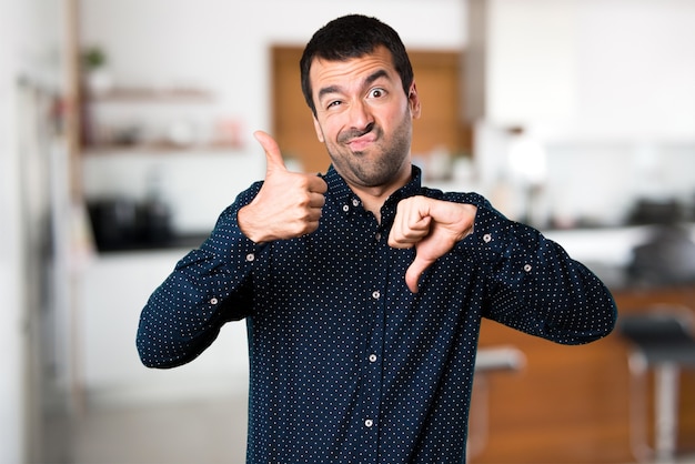 Foto hombre guapo haciendo signo bueno-malo dentro de la casa