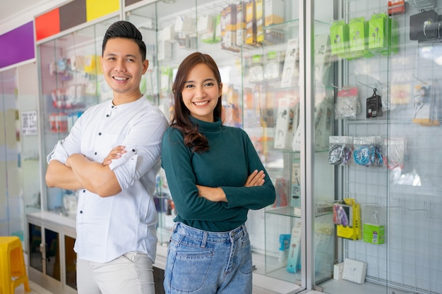 Hombre guapo y hermosa mujer sonriendo con las manos cruzadas cerca de la vitrina de accesorios de teléfono celular